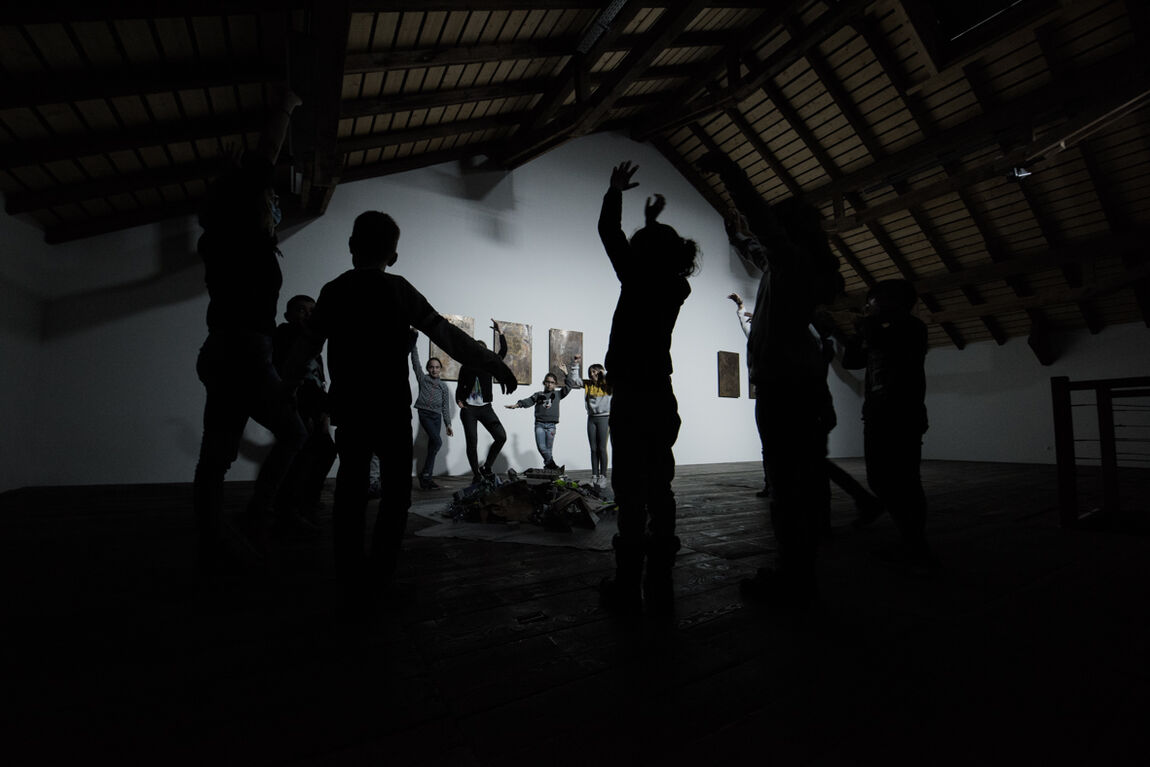 Un groupe d'enfants dansant autour d'un tas de bois sur un grand genier presque dans le noir. 
