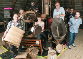 Auf dem Dachstock eines alten Gebäudes aus Holz posieren vier Männer und drei Frauen mit alten Körben, Koffern und Gefässen aus Holz und lachen in dien Kamera.